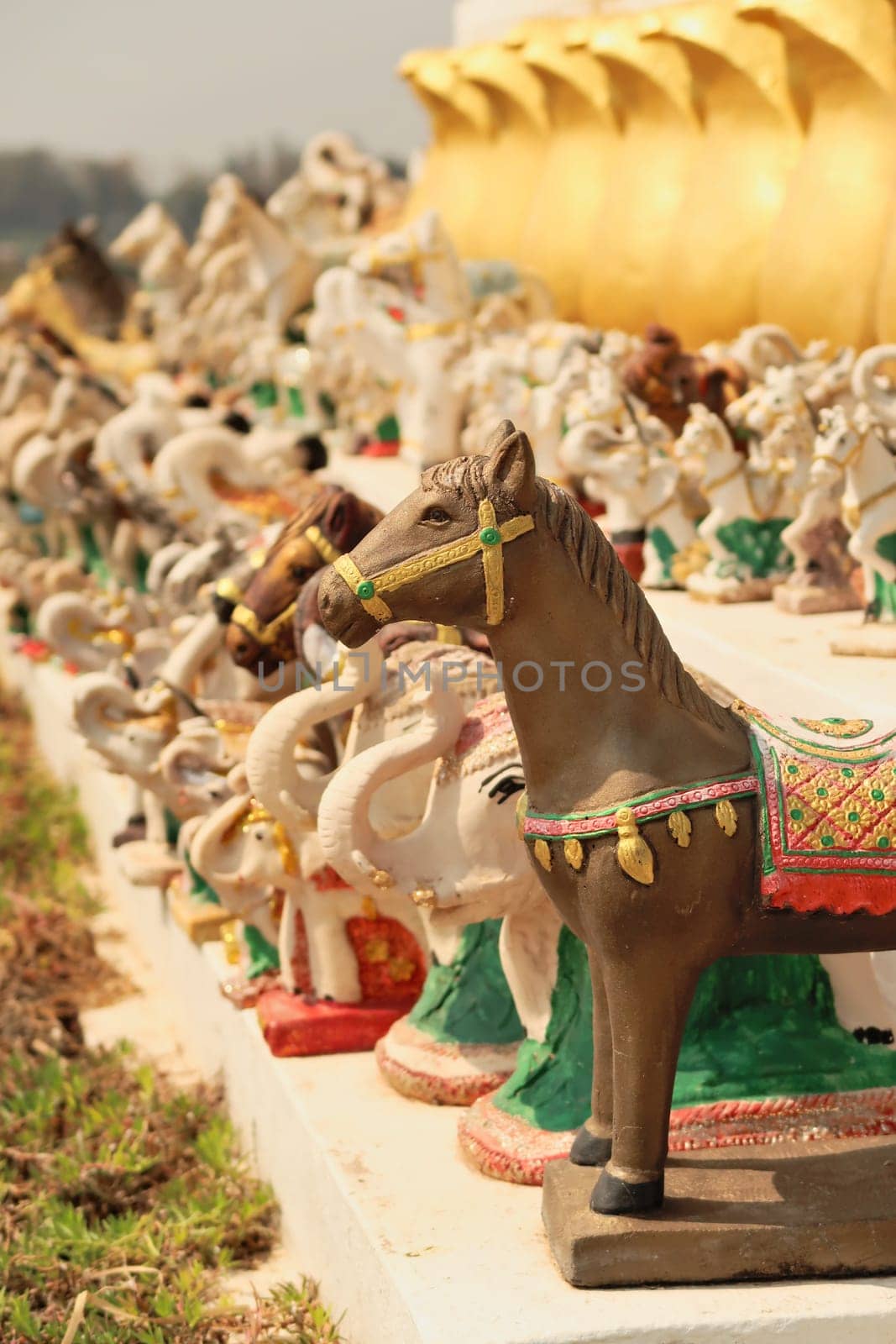Many horse and elephant statues, porcelaine figurines, figures, ceramic sculptures are lined up in a row next to the statue of King Chao Anouvong in Vientiane, Laos 2023