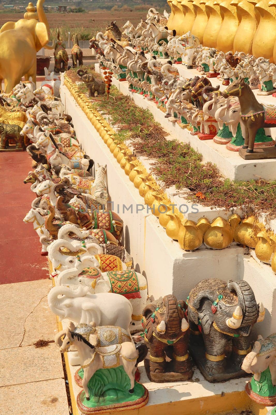 Many elephant and horse statues, porcelaine figurines, ceramic sculptures are lined up in a row next to the statue of King Chao Anouvong in Vientiane, Laos 2023