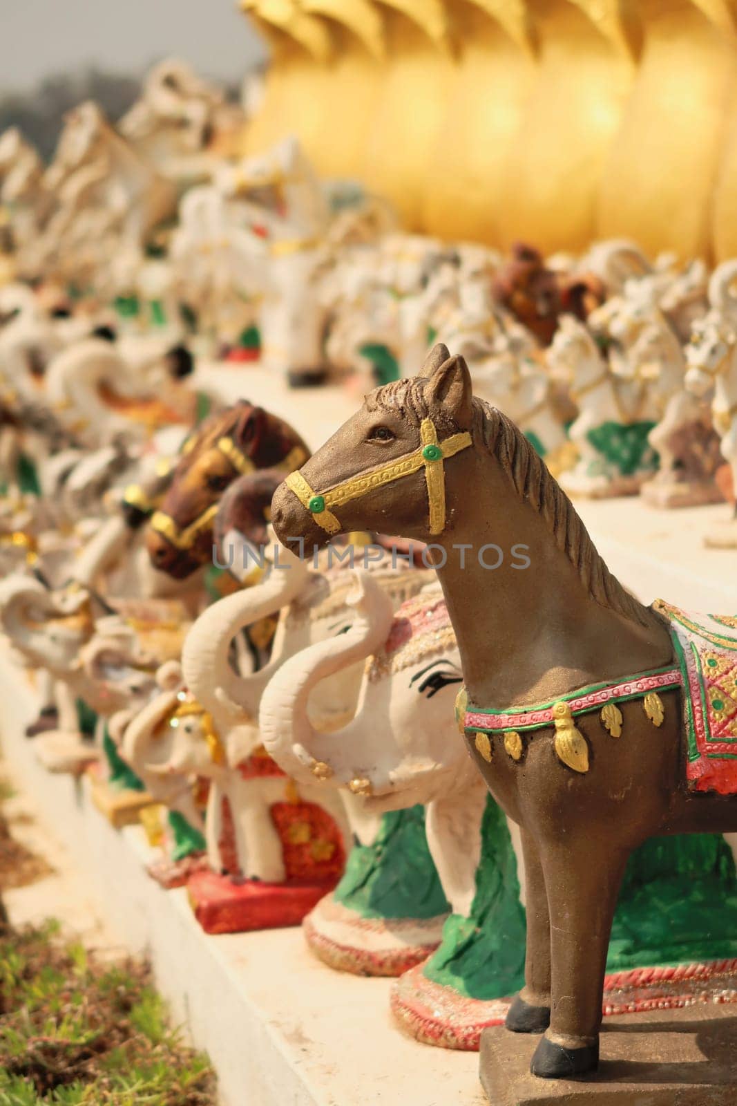 Many horse and elephant statues, porcelaine figurines, ceramic sculptures are lined up in a row next to the statue of King Chao Anouvong in Vientiane, Laos 2023