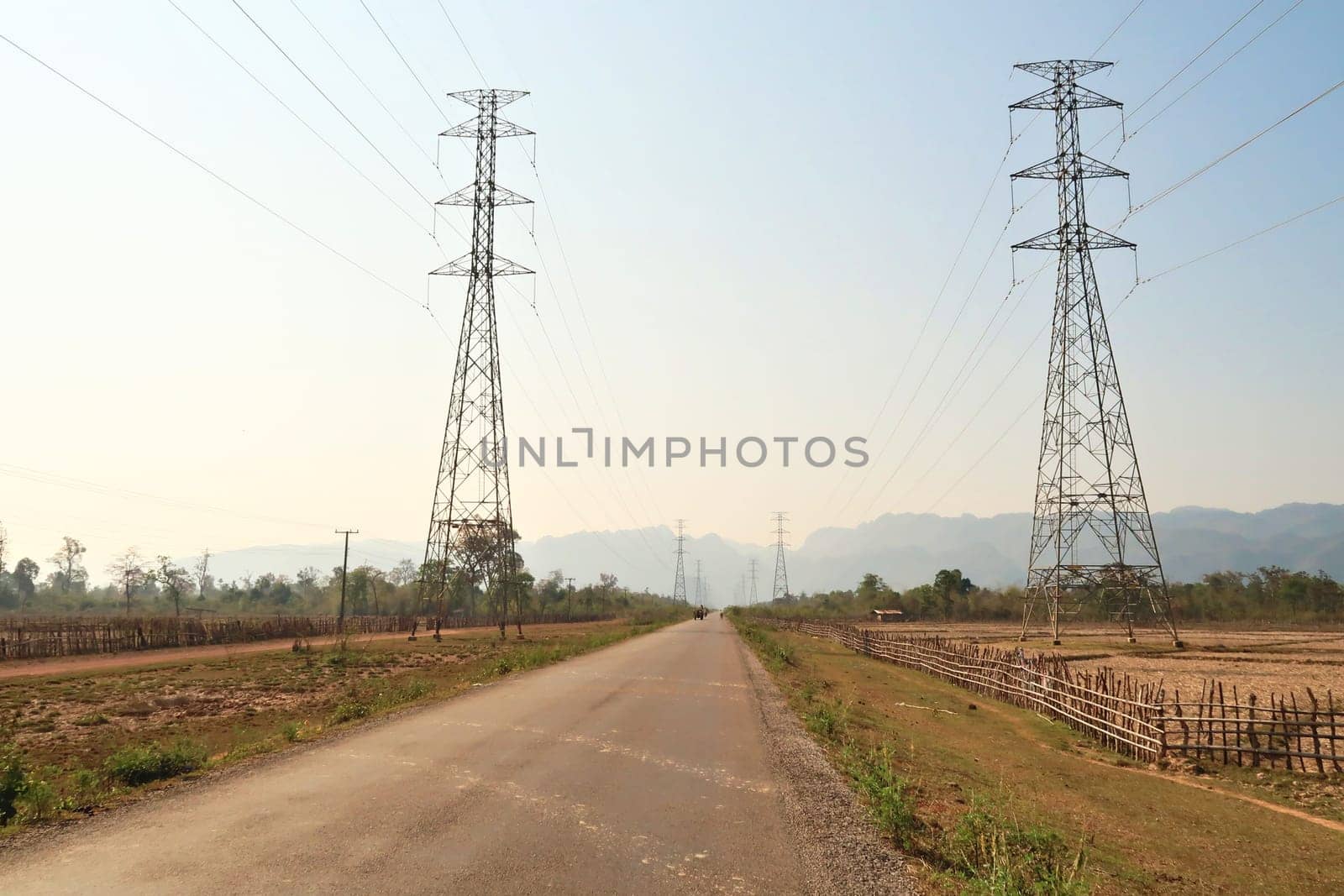 On the Thakhek Motorbike Loop in dry season, the road runs through dried out farmland next to high electricity poles, Laos 2023