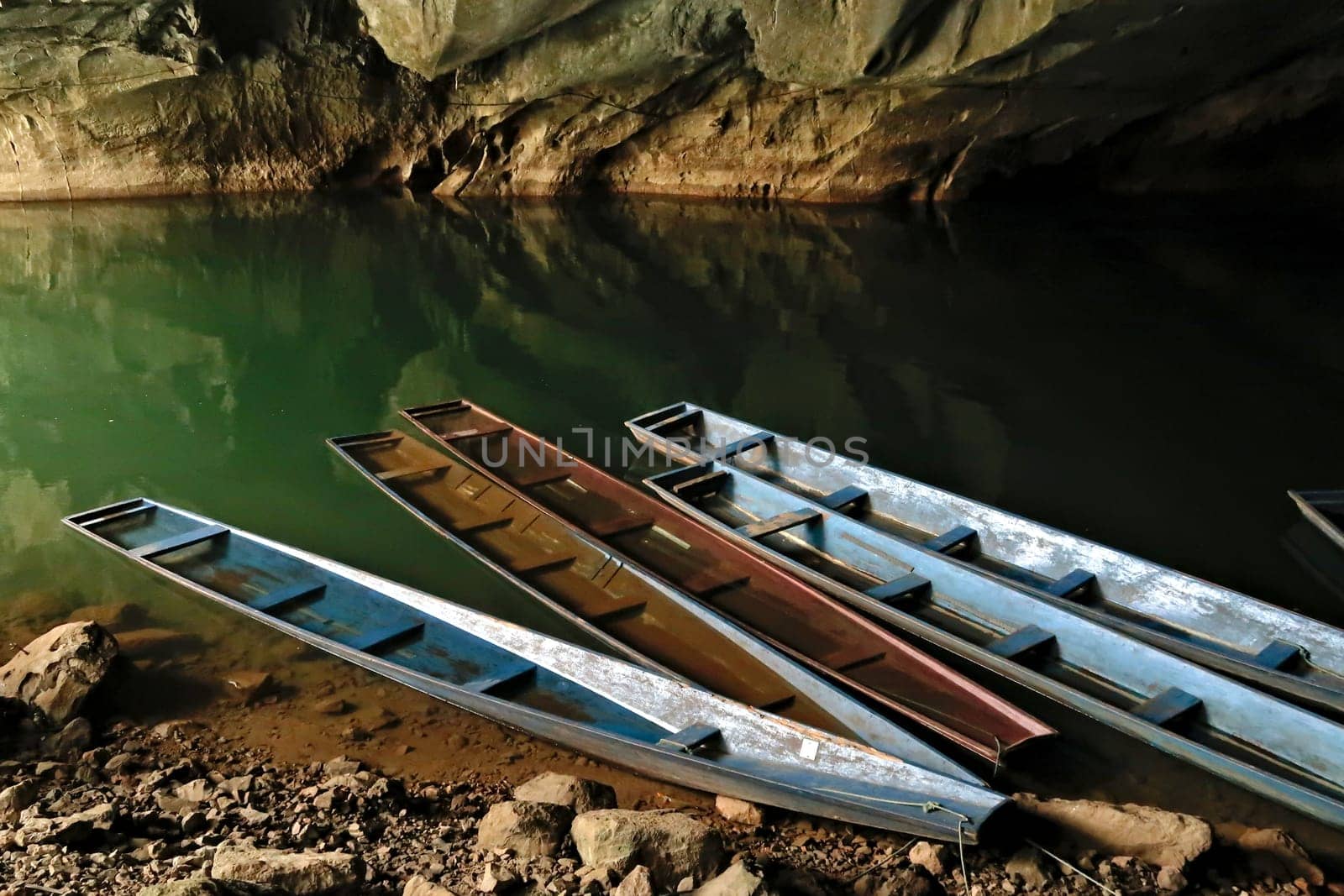 A few long boats, some of them partly submerged, sunken at the entrance of Kong Lor Cave, a tourist attraction on the Thakhek Motorbike Loop, Laos 2023