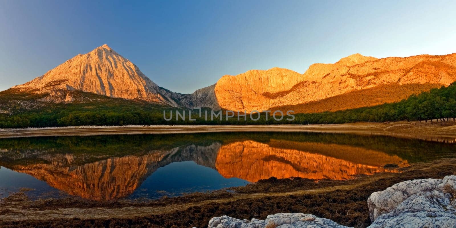 Scenic view of a mountain range reflected in a calm lake during sunrise, with golden hues illuminating the peaks.