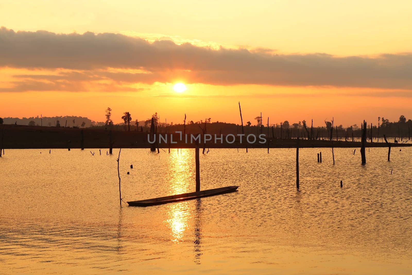 Watching the sunset over the flooded forest, trees, reservoir lake of Nam Theun, a boat is tied to one of the dead trees, village of Thalang, Thakhek Motorbike Loop, Laos 2023