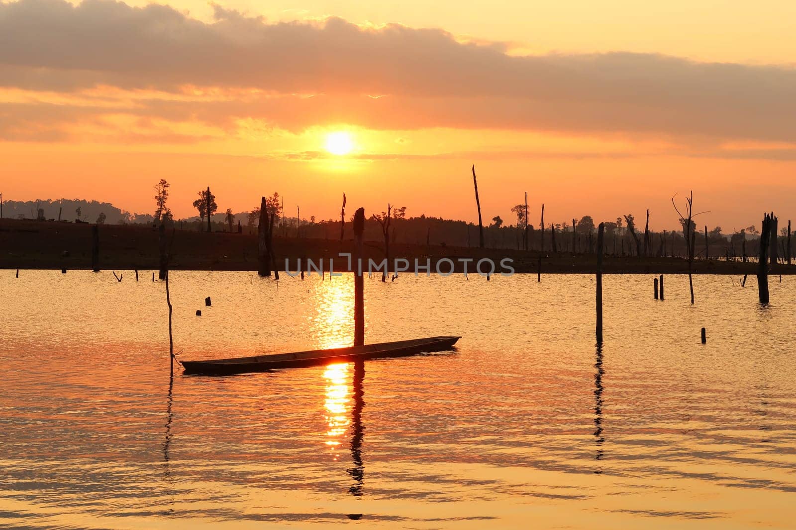 Watching the sunset over the flooded trees, forest, reservoir lake of Nam Theun, a boat is tied to one of the dead trees, village of Thalang, Thakhek Motorbike Loop, Laos 2023