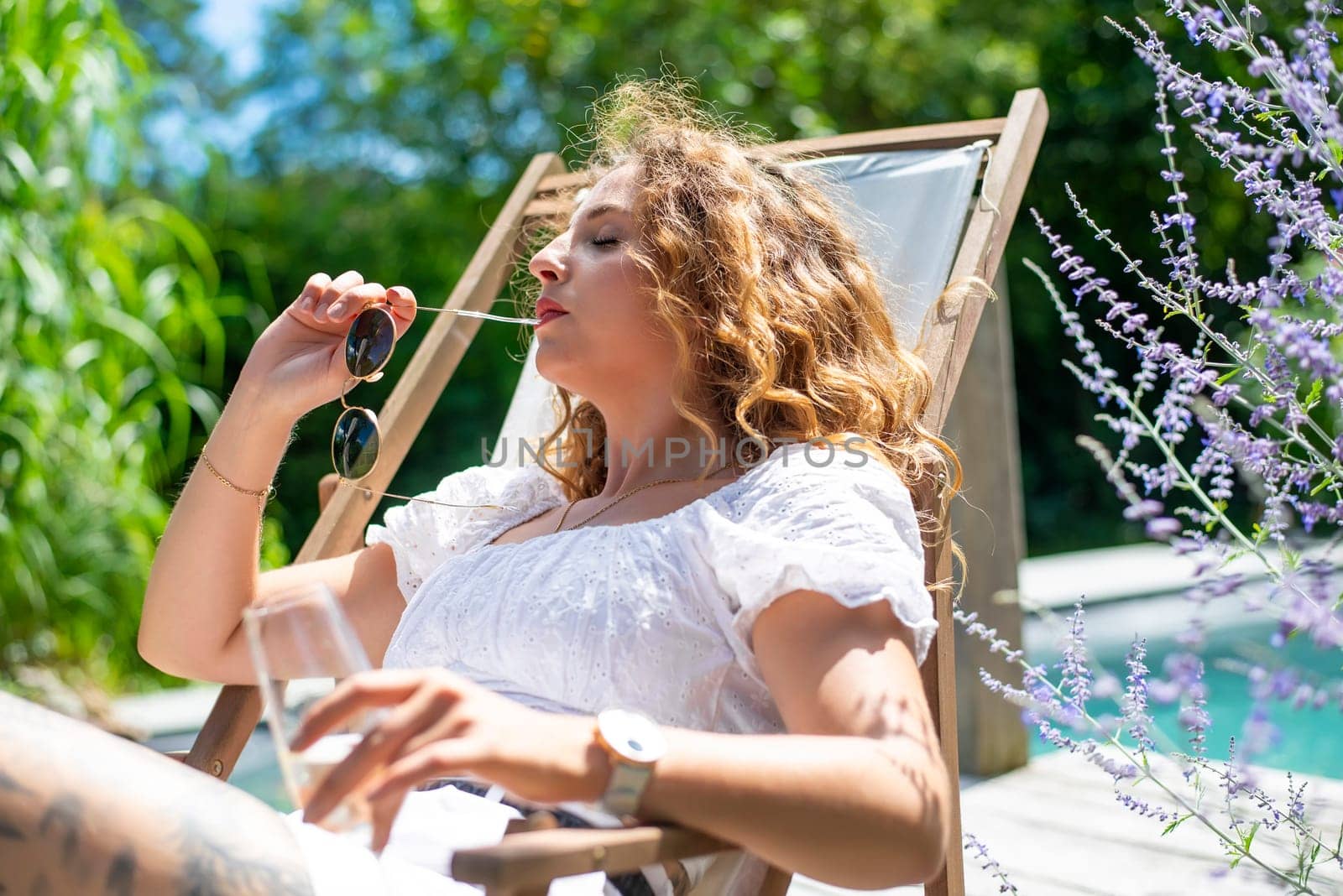 pensive young woman with sunglasses lying in a deck chair and drinking champagne