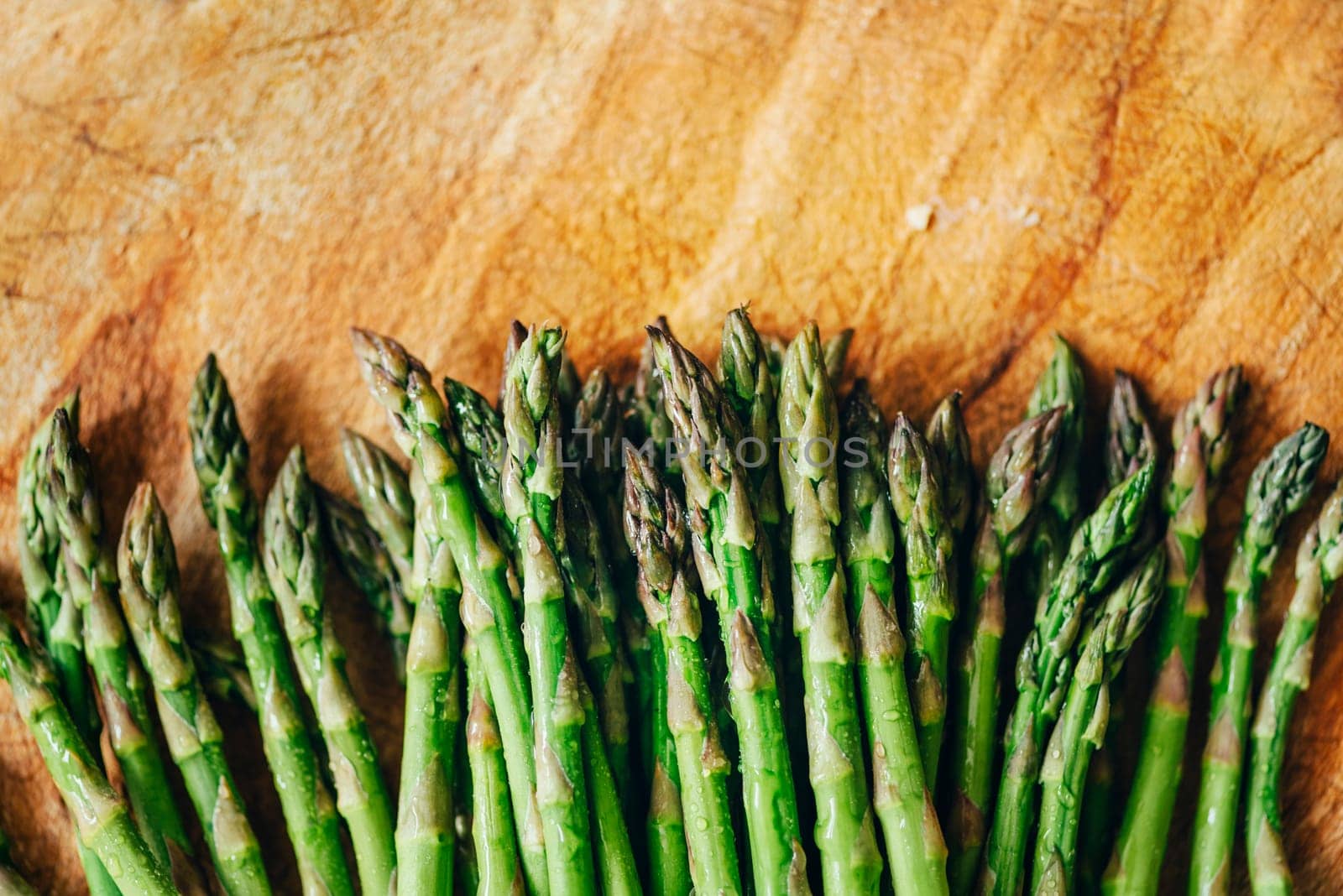 Top view of fresh green asparagus border on vintage wooden table. Cooking vegetarian food with organic ingredient on rustic board from aobve. Healthy vegetable salad recipe preparation.