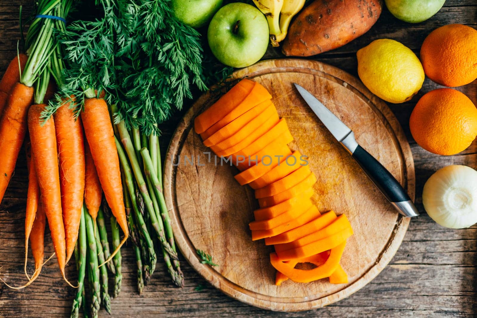 Top view of healthy bio food ingredients for smoothie preparation on wooden table. Organic superfood groceries cooking from above. Colorful fruits and vegetables in kitchen background. Butternut squash, carrots, sweet potato, oranges, apples, carrots and asparagus on cutting board overhead.
