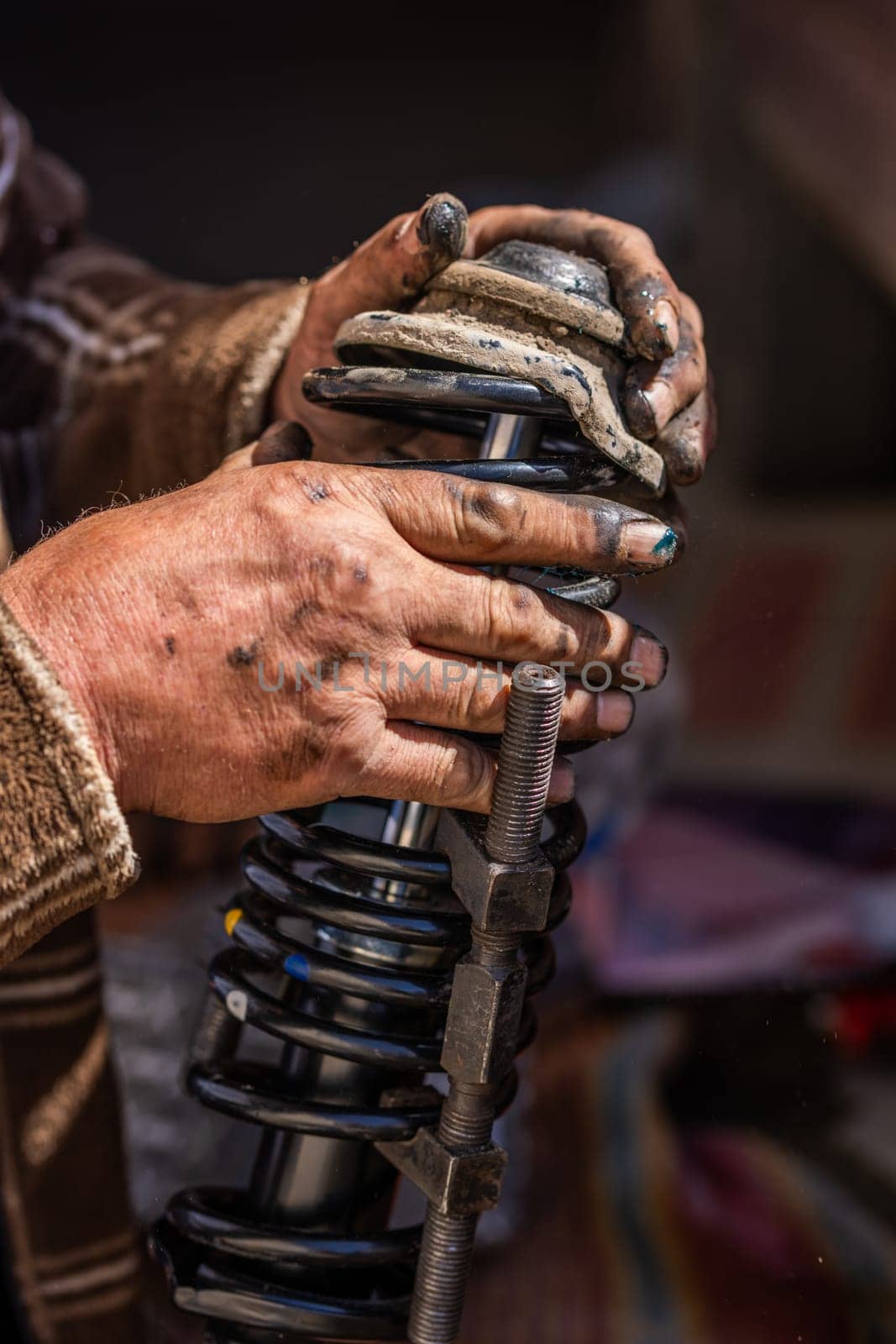 Dirty and calloused hands of a mechanic assembling compressed coil spring during DIY car repairs. Closeup.