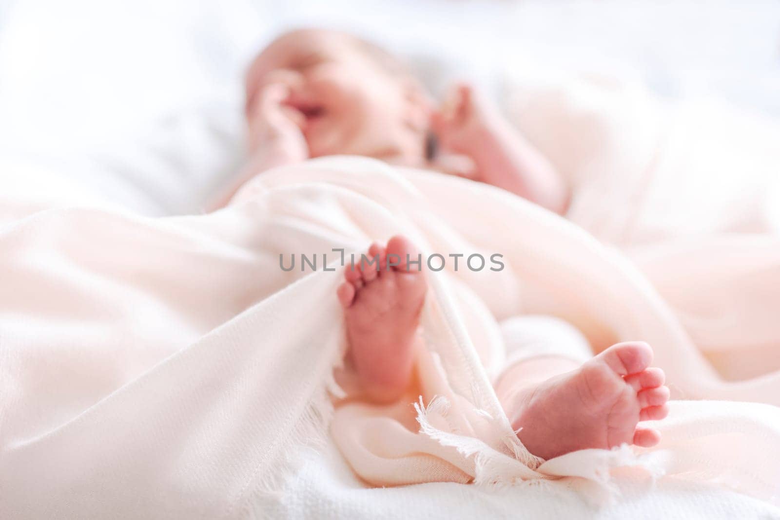 Cute newborn baby in white soft blanket after bath. Closeup of infant foot and blur pastel background. Child skincare and health care.