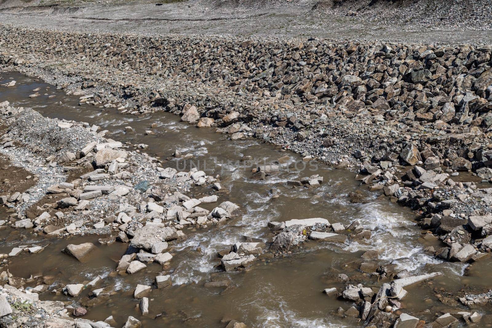 shallow river canal reinforced with large stone embankments at sunny day