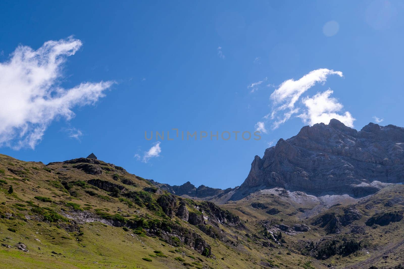 A mountain range with a clear blue sky in the background. The sky is dotted with clouds, giving the scene a serene and peaceful atmosphere