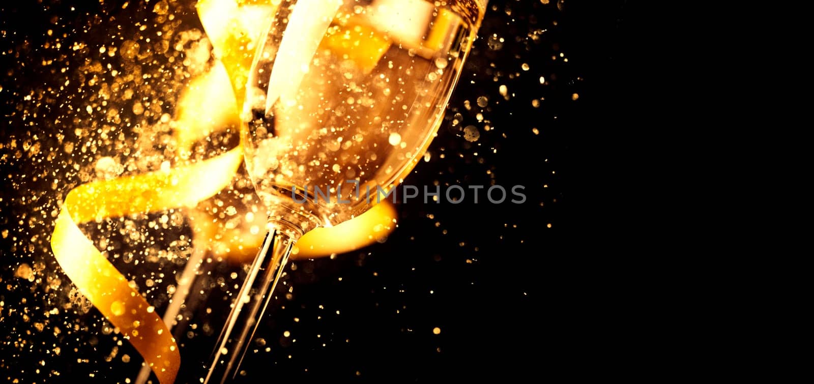Two champagne glasses with golden ribbon and gold glitter splash bokeh on dark background. Luxury restaurant dinner celebration. Classy christmas and new year holiday panoramic design banner.