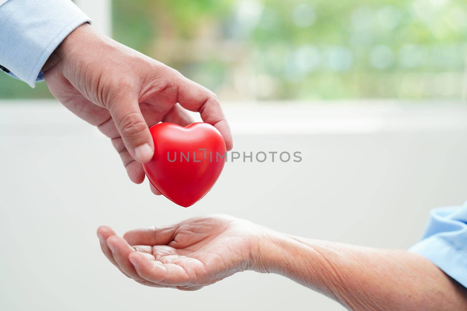 Asian elder senior woman patient holding red heart in hospital.