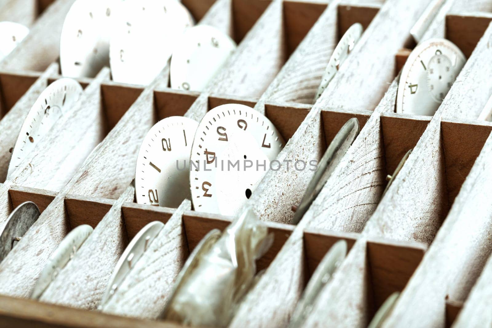 Watch dials in a wooden organizer tray display careful arrangement, highlighting the watch repair shop's need for efficient storage of components in a highly organized, accessible manner