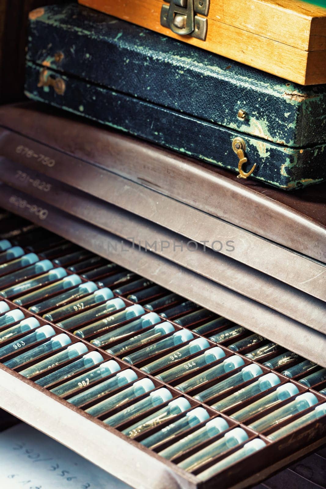 Organized drawer displays labeled tubes holding watch parts, with two vintage cases stacked above. The meticulous layout and aged cases evoke a sense of tradition in watchmaking