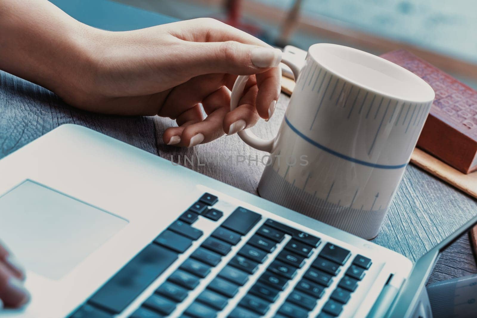 close-up of a hand with manicured nails pressing a laptop key, set against a cool-toned background with a coffee cup, emphasizing focus and productivity