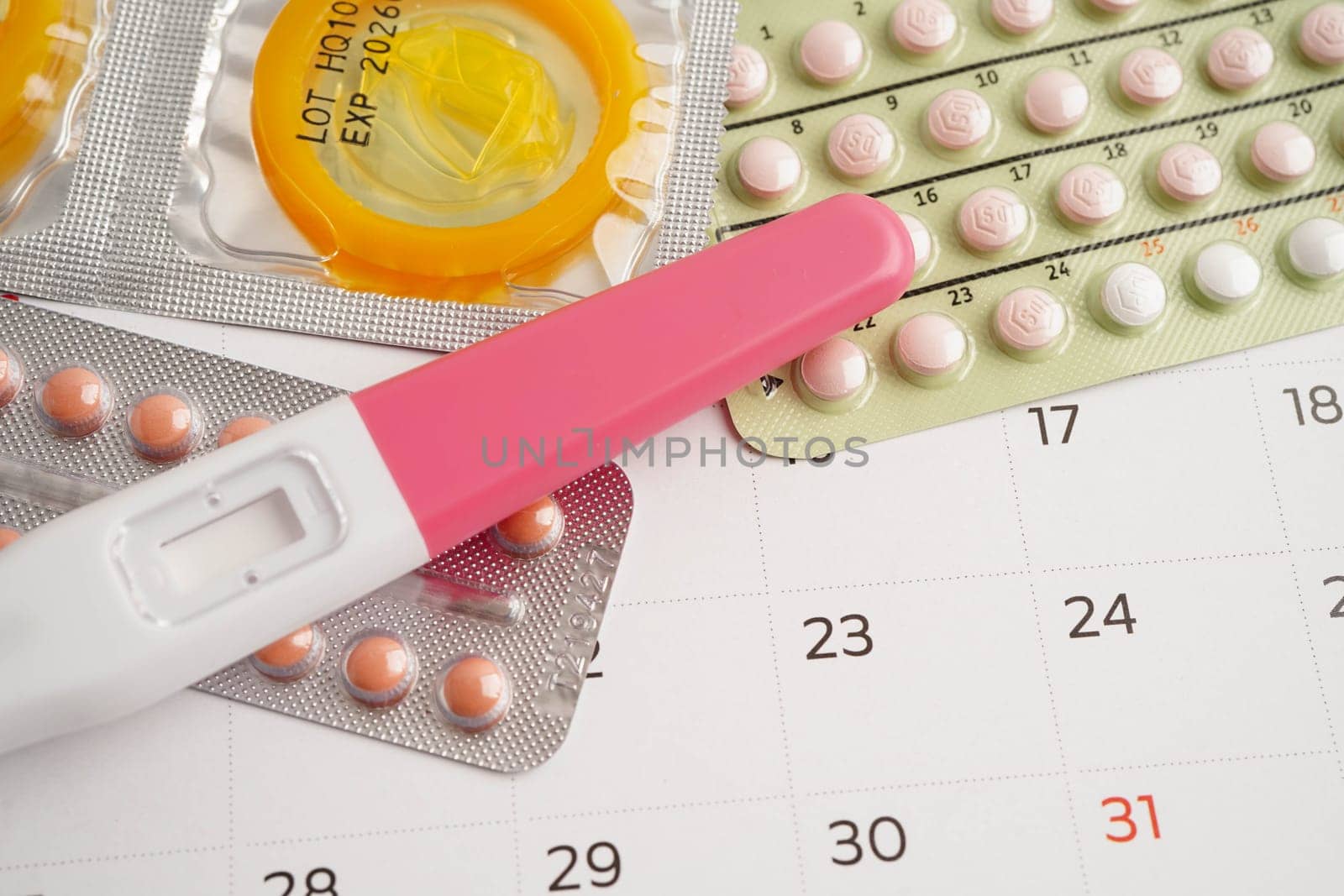 Pregnancy test with birth control pills and condom for female on calendar, ovulation day.