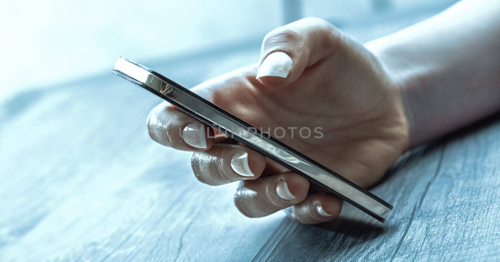 close-up image of a hand holding a smartphone in a relaxed grip. The hand features light skin and well-manicured nails, suggesting a calm atmosphere with soft natural lighting