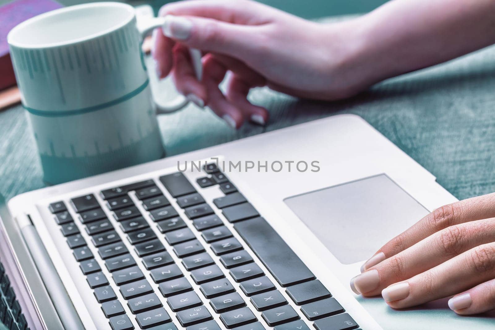 Light-skinned hand with polished nails gently pressing a laptop key. A blurred coffee cup in the background creates a calm workspace, focusing on precision and productivity