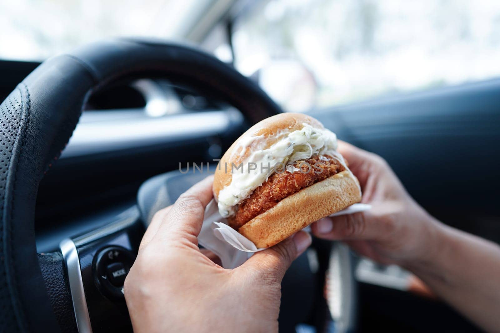 Asian woman driver hold and eat hamburger in car, dangerous and risk an accident.