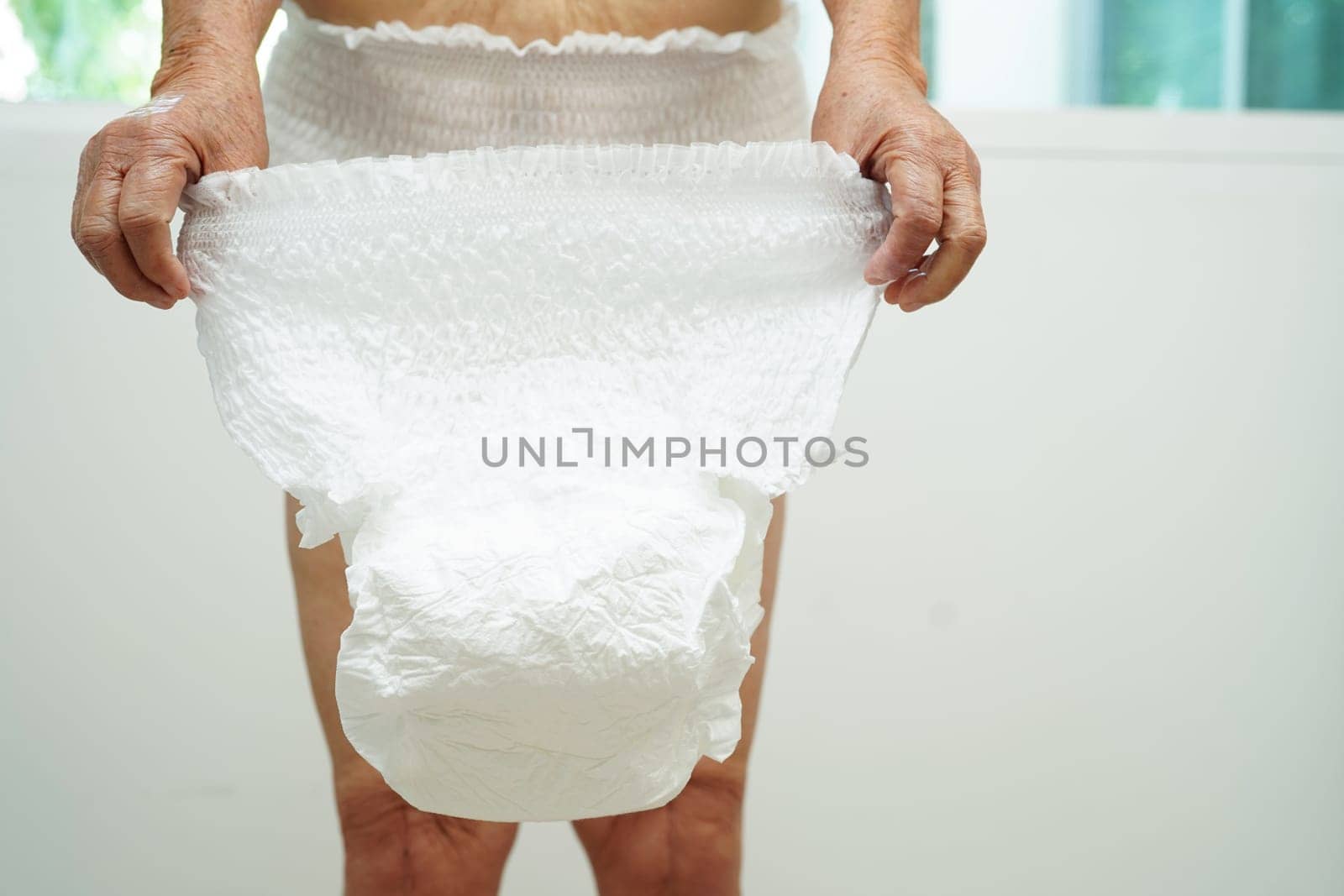 Asian senior woman patient wearing adult incontinence diaper pad in hospital.