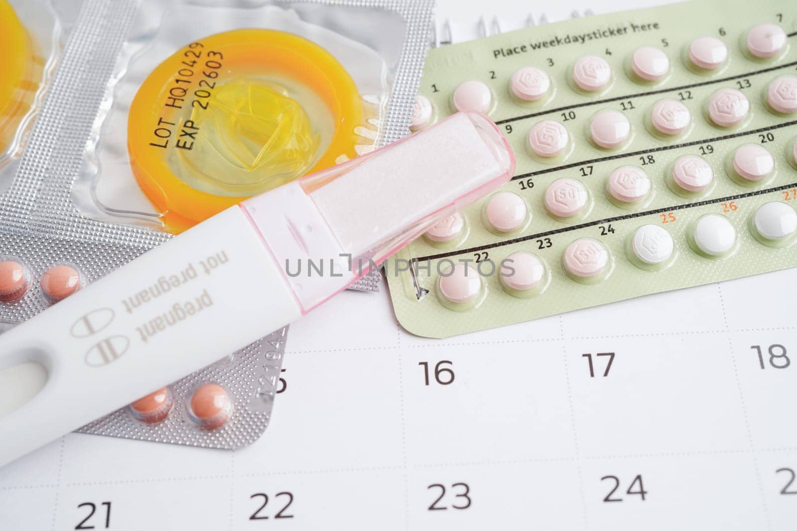 Pregnancy test with birth control pills and condom for female on calendar, ovulation day.