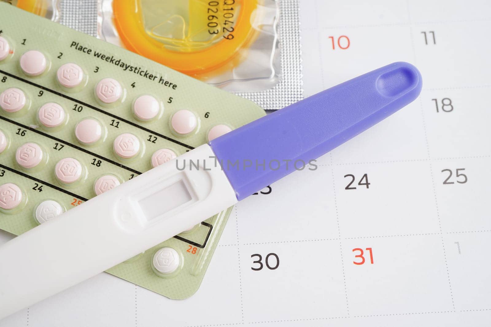 Pregnancy test with birth control pills and condom for female on calendar, ovulation day.