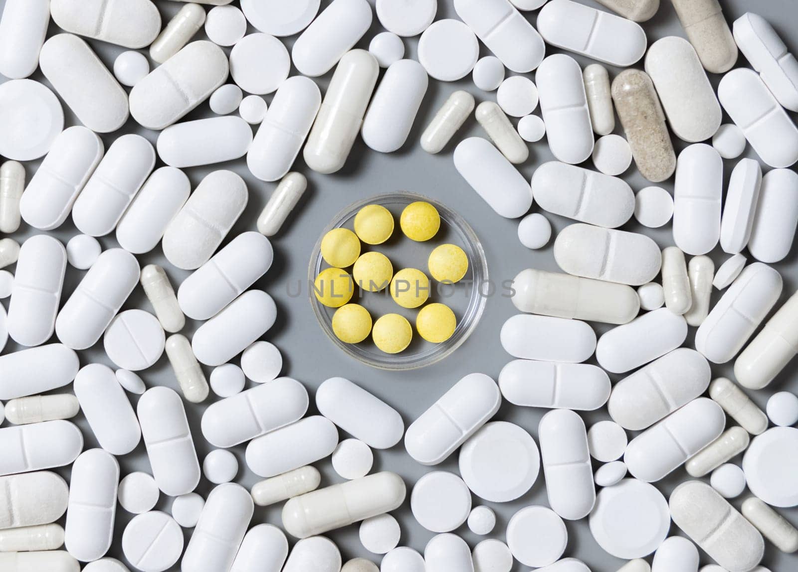Mix of white medical capsules and pills with yellow pills in the middle on grey top view. Medicinal treatment. Taking dietary supplements. Assorted pharmaceutical products