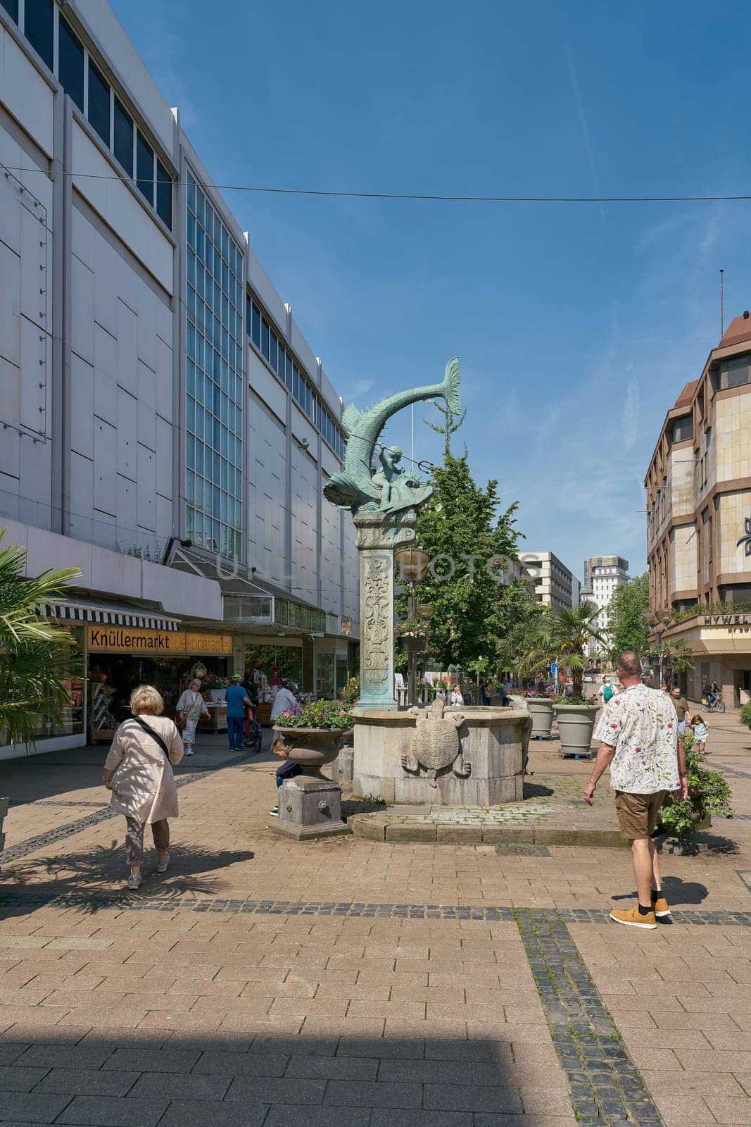 Pedestrian zone with the Triton Brunnen, Triton fountain from 1902 and some passers-by in the city center of Duisburg in Germany
