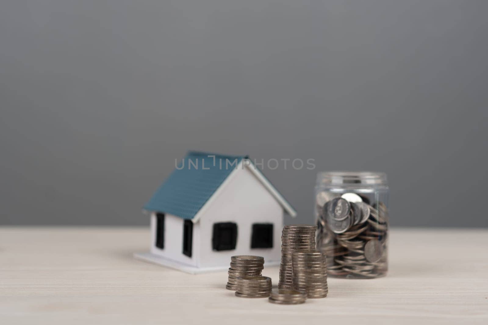 house model beside stacks of coins and a jar filled with money savings, real estate investment, and financial planning for property ownership.