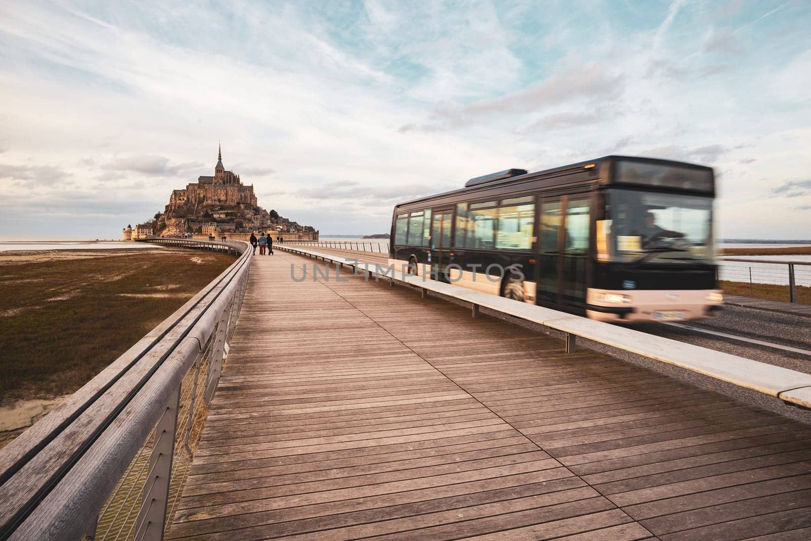 Mont Saint-Michel, France - February 25, 2024: Mont Saint-Michel and shuttle bus with tourists photographed in winter from the long bridge in Normandy, France