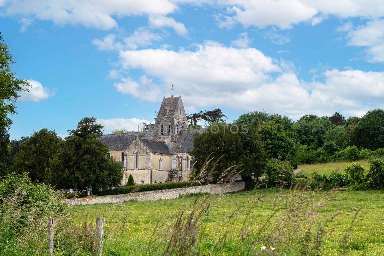 A church with a steeple sits in a grassy field. The sky is clear and blue, and the sun is shining brightly. Normandy, France