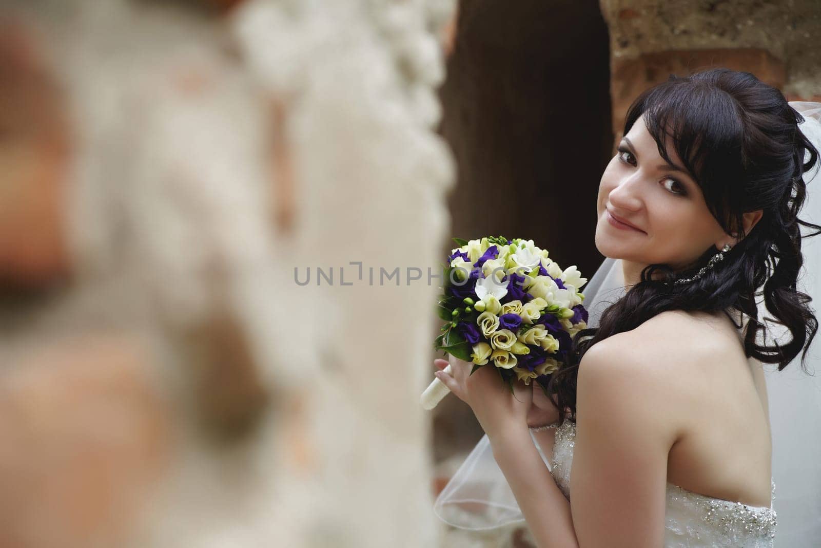 Stunning bride elegantly poses with her bouquet in the ruins of an old fortress outdoors