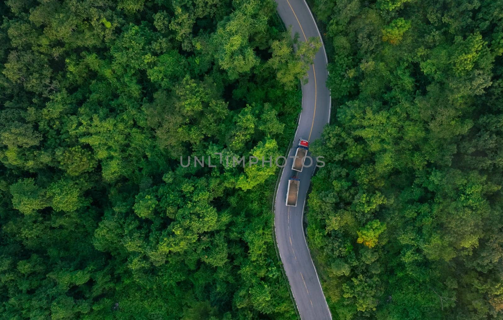 Aerial view of hydrogen energy truck driving on highway road in green forest. Sustainable transportation. Blue truck driving on asphalt road in forest. Hydrogen fuel cell vehicle. Zero emission car.