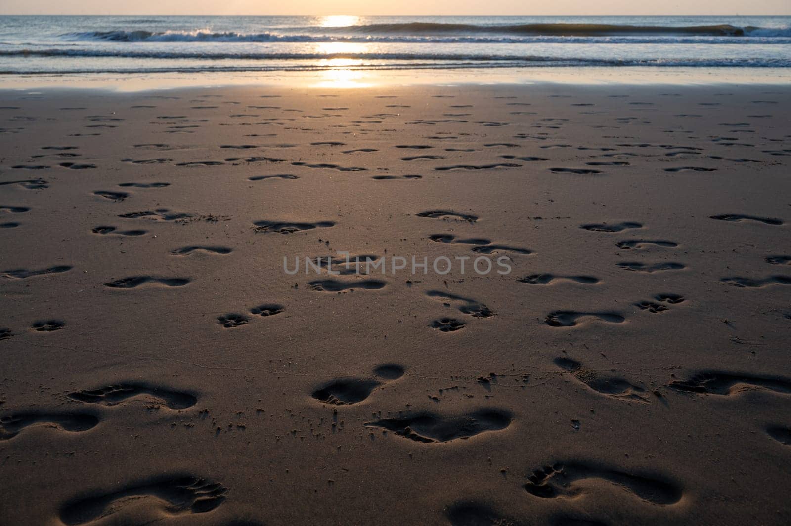 Many footprints in the wet sand by the sea, in the evening light with sea and sunlight