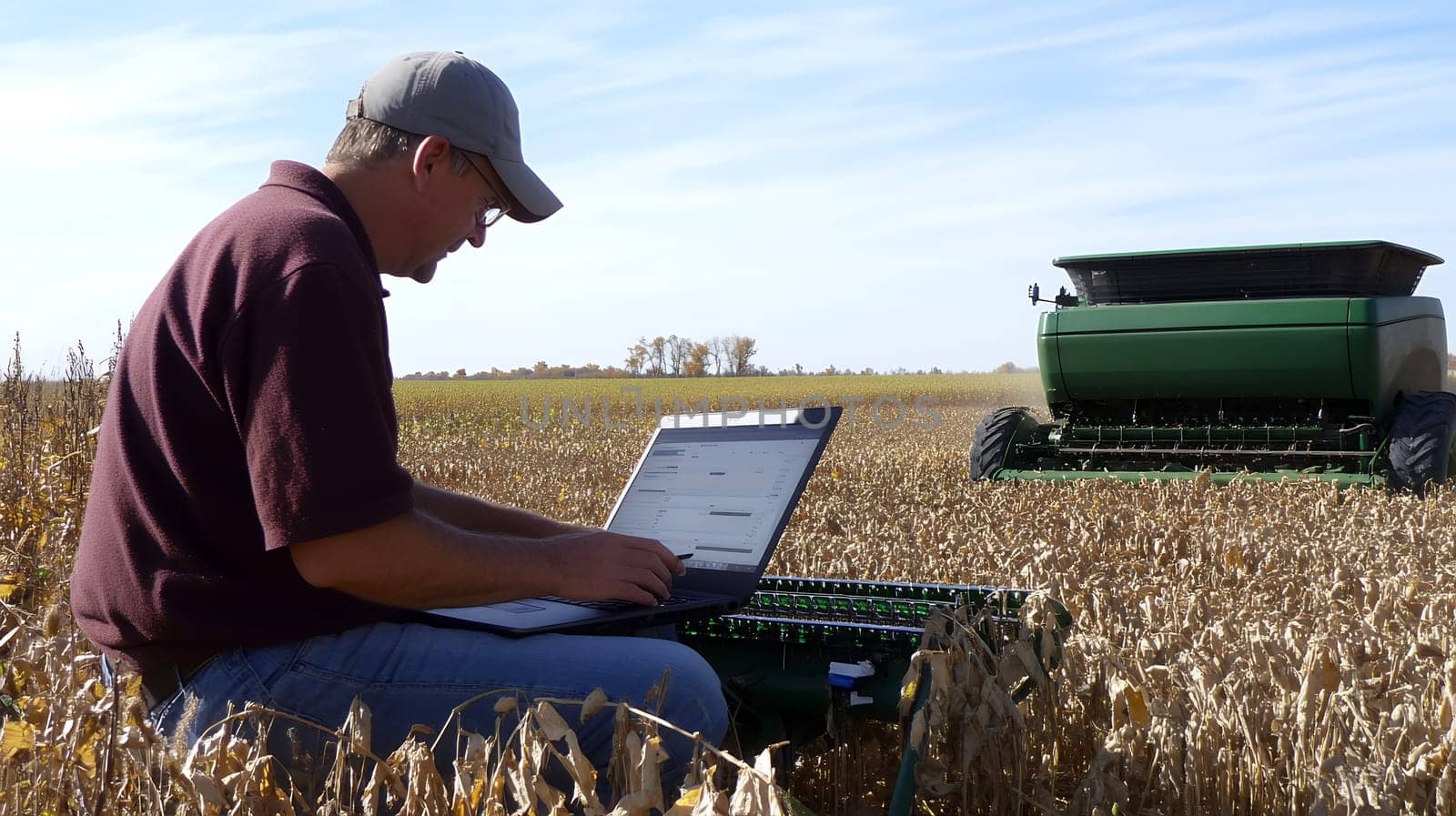 A farmer uses a laptop in a vast field, integrating technology with traditional agriculture practices.