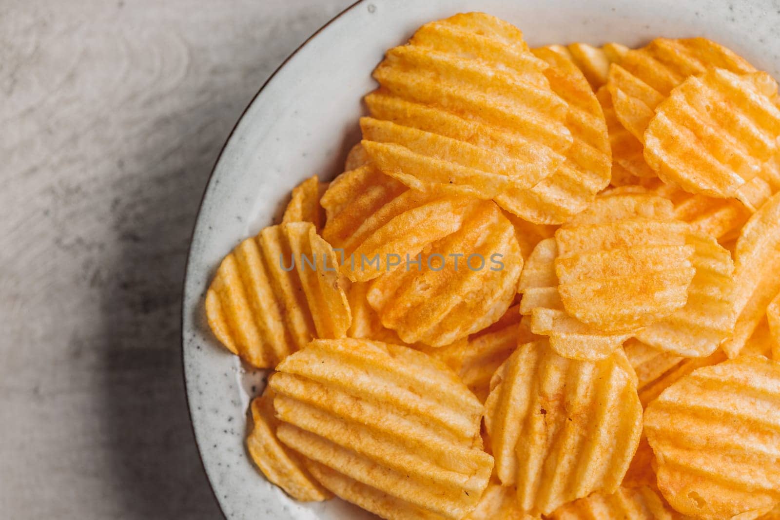 Crispy potato chips on plate on a kitchen table. Top view.