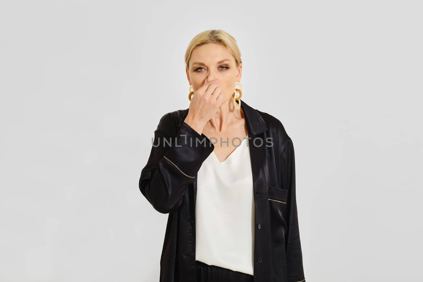 Woman with a cold wipes her nose with her hand standing against a neutral grey backdrop