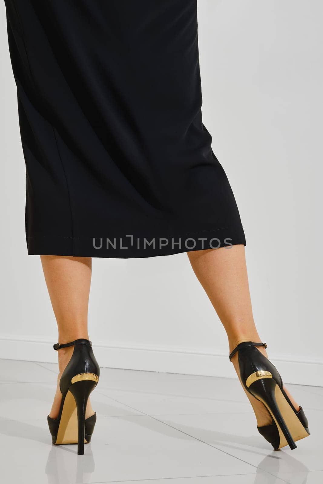 Rear view of a stylish high heels worn by a woman dressed in a black outfit