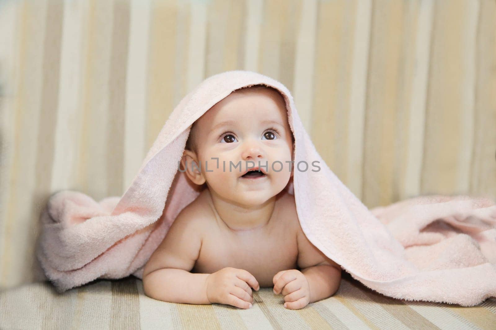 An adorable baby is looking up with wonder while being covered snugly by a soft pink blanket thats cozy