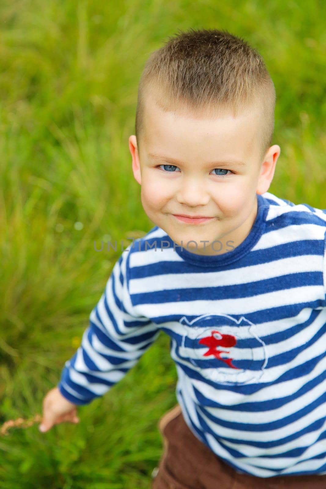 A joyful little boy with a big smile and a striped T-shirt is playing outside