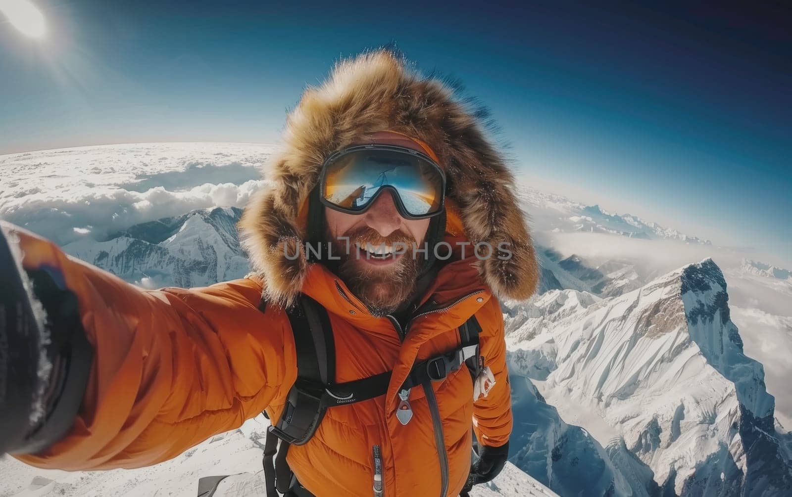 Ecstatic mountaineer in orange gear celebrates at the snow-covered peak with a selfie, vibrant against the backdrop of clear blue skies