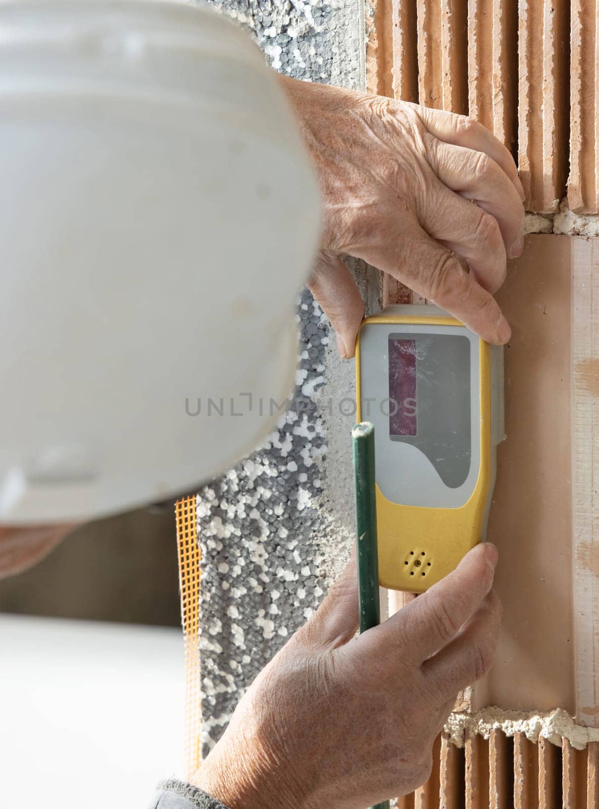 Craftsman in white helmet and grey dusty working clothing measuring with horizontal rotary laser level. Engineer during measurement work, construction or renovation site