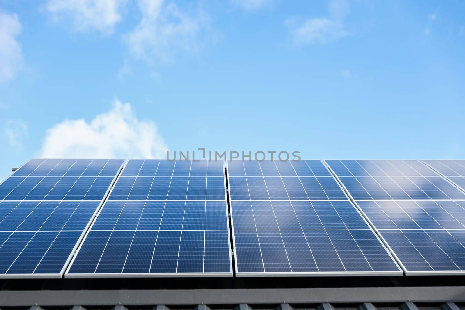 Solar panel cells on cloudy blue sky background. Clean alternative energy power concept. Modern house with solar panels stand-alone photovoltaic plant system on metal sheet roof. Go green
