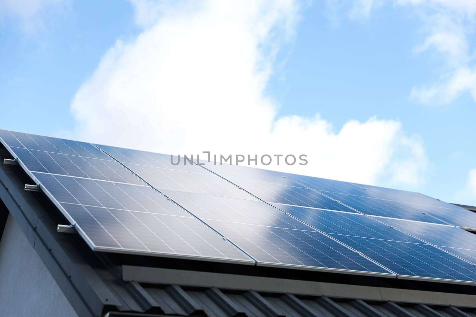 Solar panel cells on cloudy blue sky background. Clean alternative energy power concept. Modern house with solar panels stand-alone photovoltaic plant system on metal sheet roof. Go green