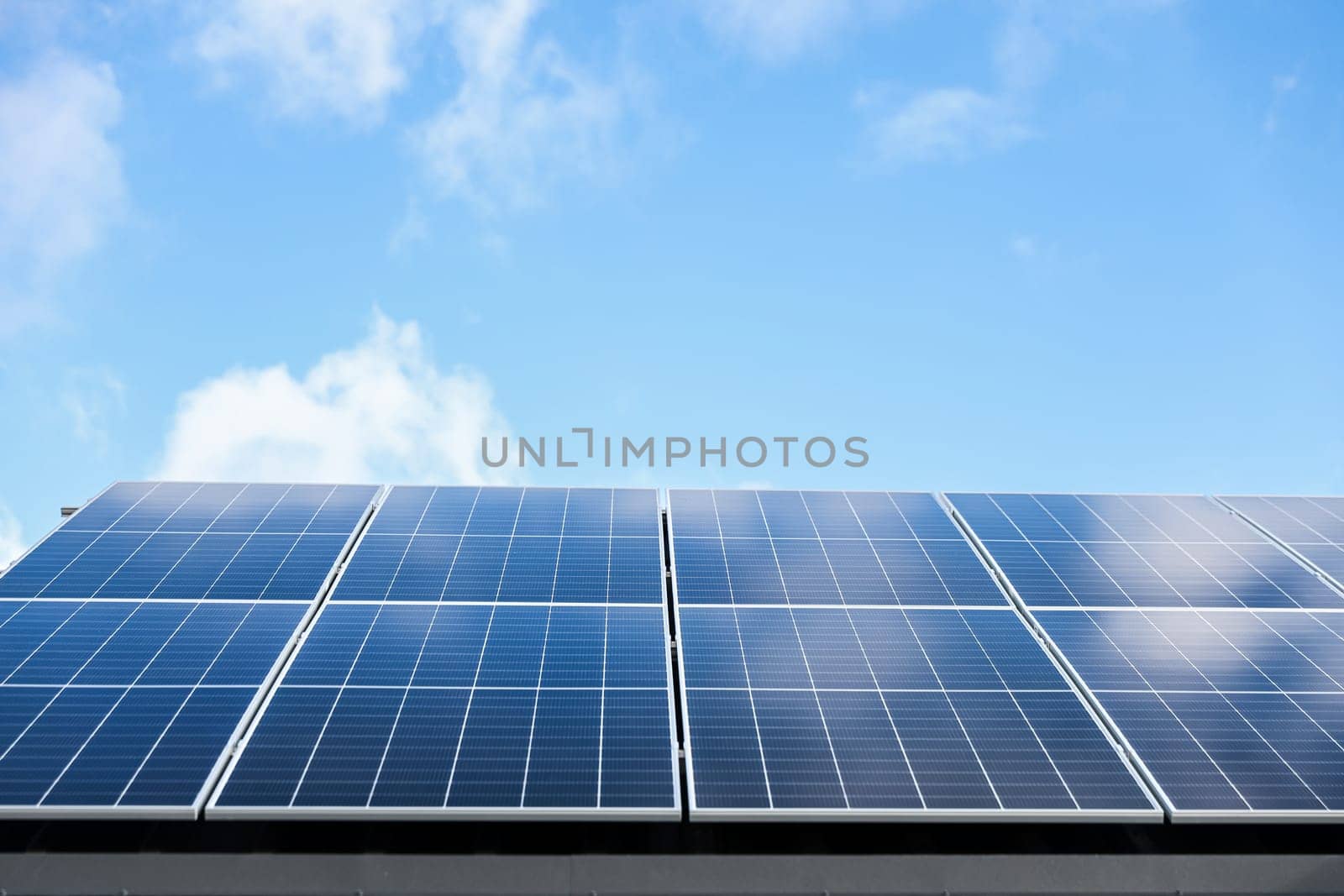 Solar panel cells on cloudy blue sky background. Clean alternative energy power concept. Modern house with solar panels stand-alone photovoltaic plant system on metal sheet roof. Go green