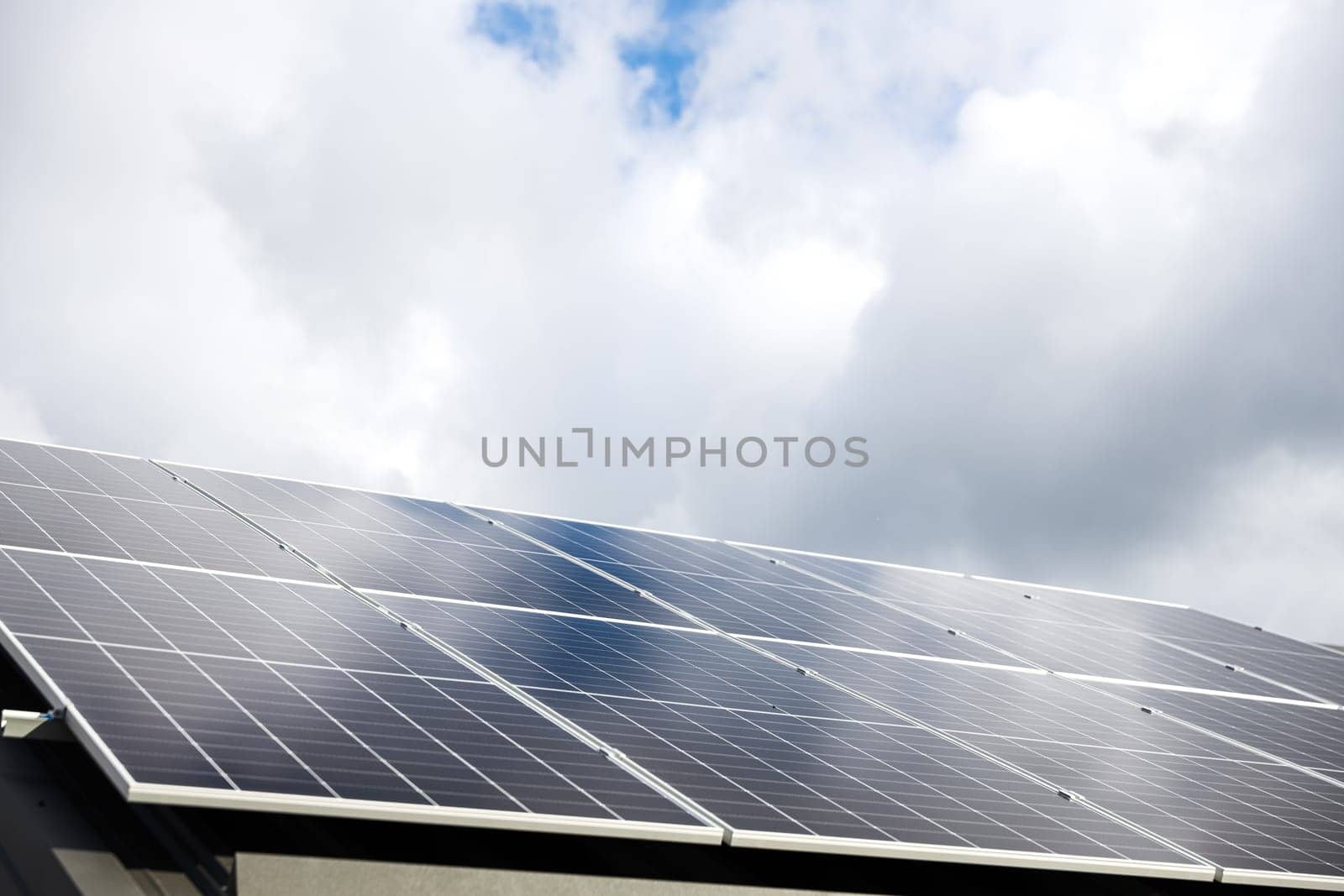 Aerial view of solar panel cells on clouds, blue sky background. Clean alternative energy power in nature concept, sustainable resources. House with solar panel photovoltaic plant system on metal roof