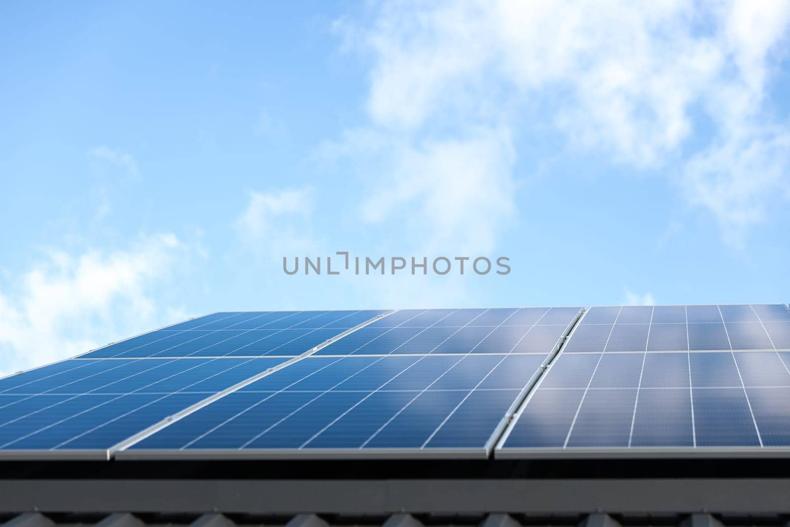 Solar panel cells on cloudy blue sky background. Clean alternative energy power concept. Modern house with solar panels stand-alone photovoltaic plant system on metal sheet roof. Go green