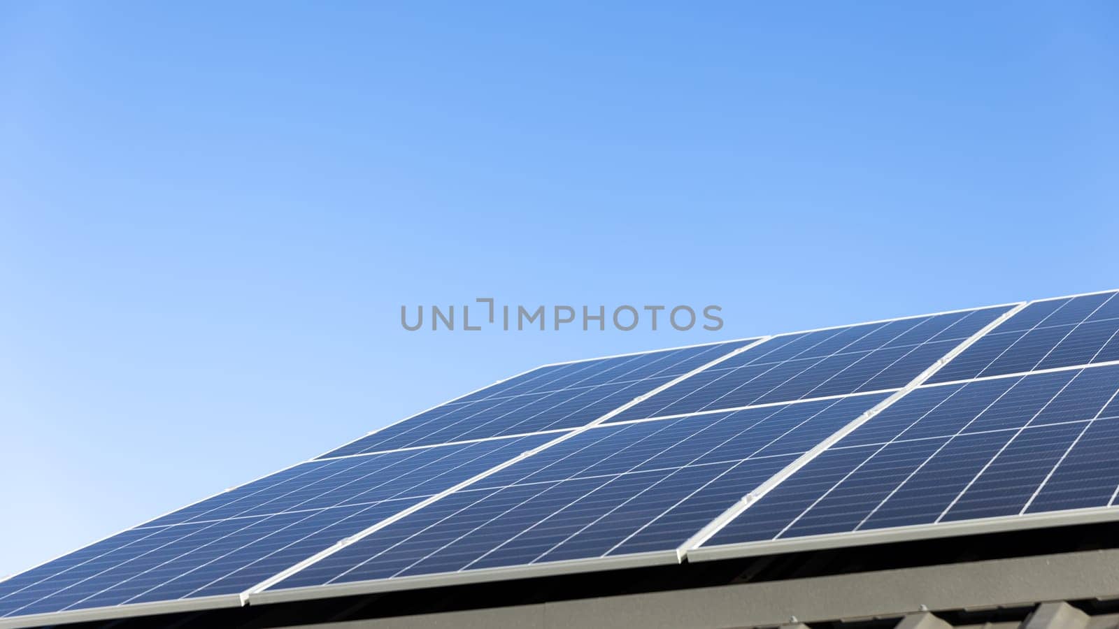 Aerial view of solar panel cells on clear blue sky background. Clean alternative energy power concept, sustainable resources. Modern house, solar panels stand-alone photovoltaic plant system on roof