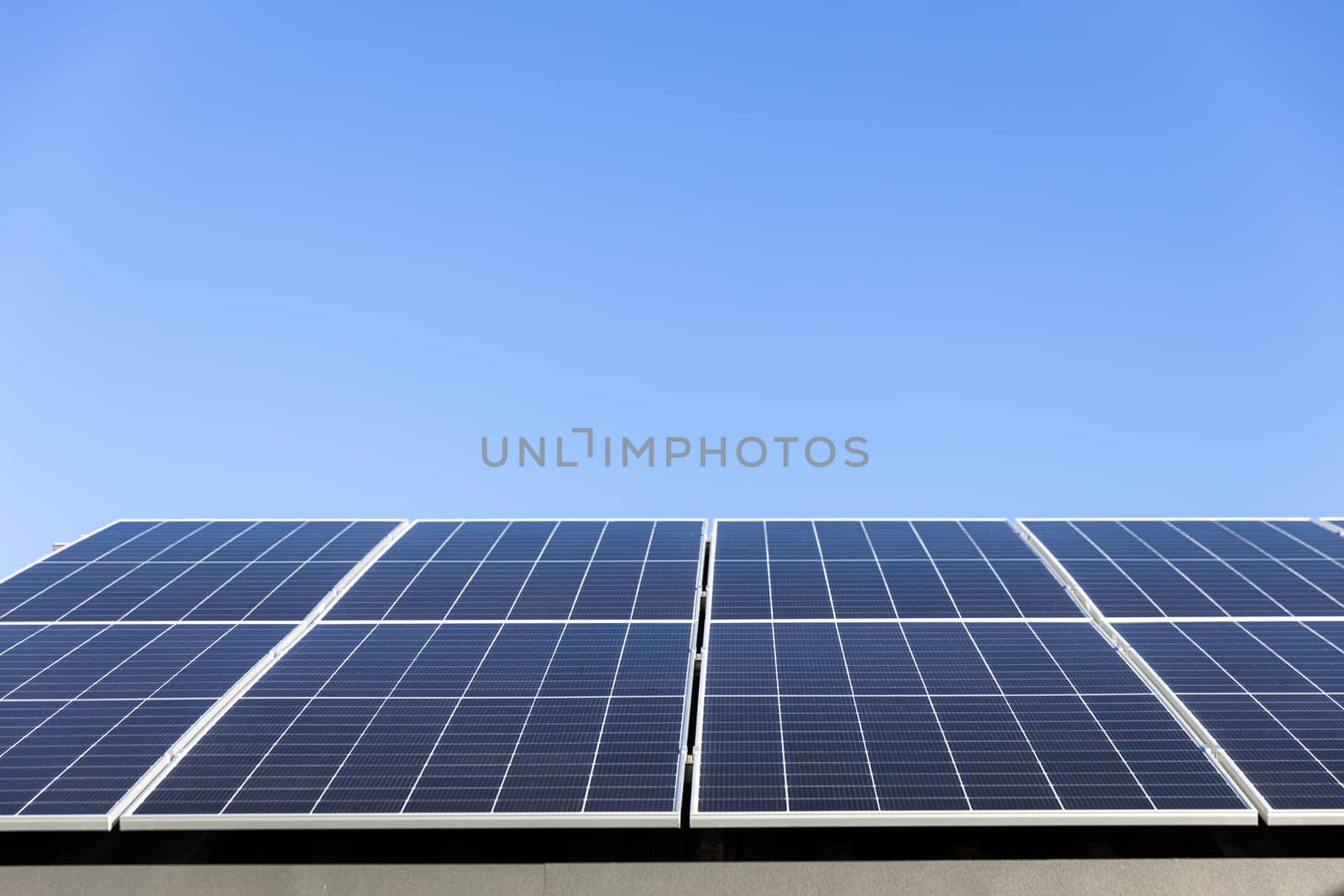 Aerial view of solar panel cells on clear blue sky background. Clean alternative energy power concept, sustainable resources. Modern house, solar panels stand-alone photovoltaic plant system on roof
